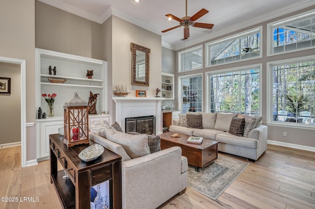 living room with crown molding, built in features, light hardwood / wood-style floors, and ceiling fan