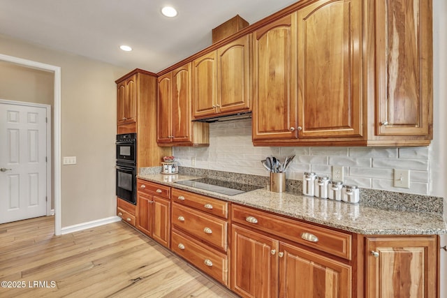 kitchen with light stone counters, light wood-type flooring, tasteful backsplash, and black appliances