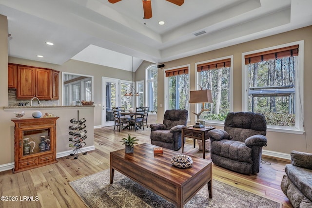 living room featuring a raised ceiling, ceiling fan, and light wood-type flooring