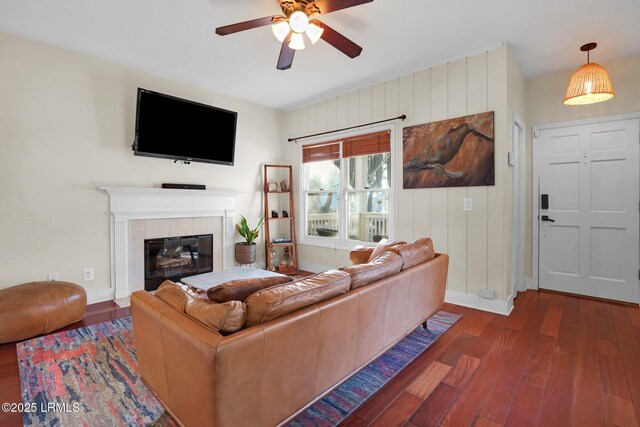 living room with a tiled fireplace, dark wood-type flooring, and ceiling fan