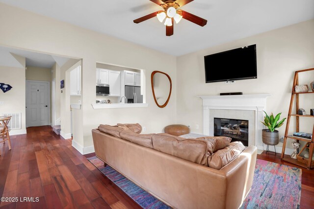 living room with a tile fireplace, dark wood-type flooring, and ceiling fan