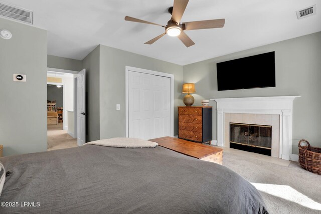 bedroom with ceiling fan, light colored carpet, a fireplace, and a closet