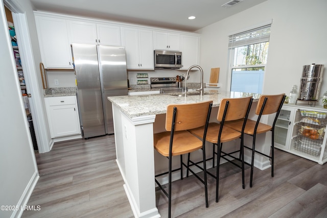 kitchen featuring a breakfast bar area, light stone counters, appliances with stainless steel finishes, a kitchen island with sink, and white cabinets