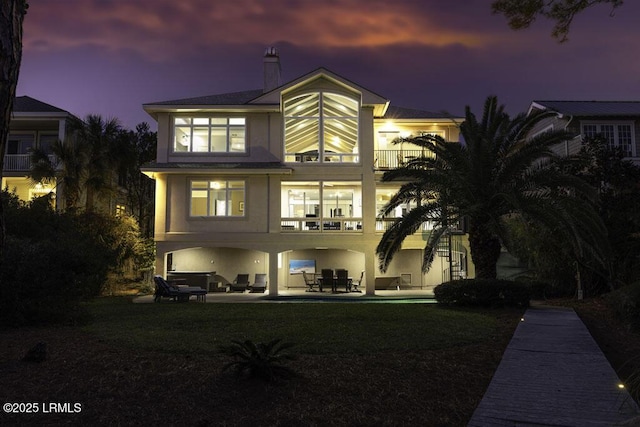 back house at dusk with a balcony, a yard, and a patio area