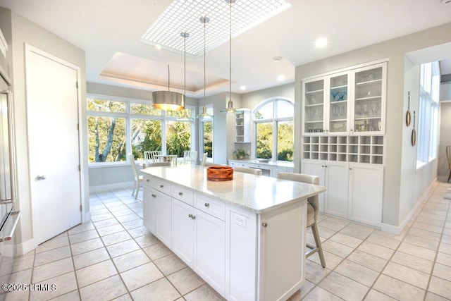 kitchen featuring a breakfast bar area, white cabinetry, hanging light fixtures, a tray ceiling, and a kitchen island