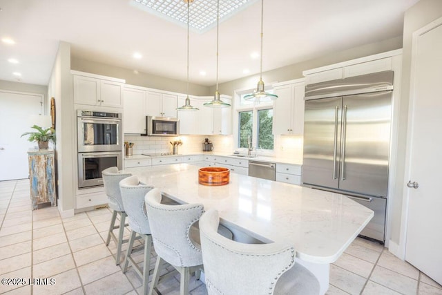 kitchen featuring stainless steel appliances, a center island, tasteful backsplash, white cabinets, and decorative light fixtures