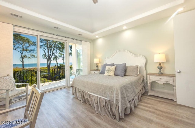 bedroom featuring a water view, access to exterior, a raised ceiling, and light hardwood / wood-style flooring