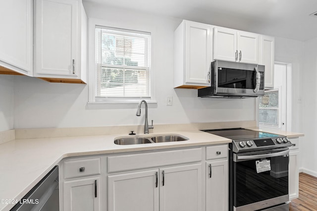 kitchen with stainless steel appliances, white cabinetry, wood-type flooring, and sink