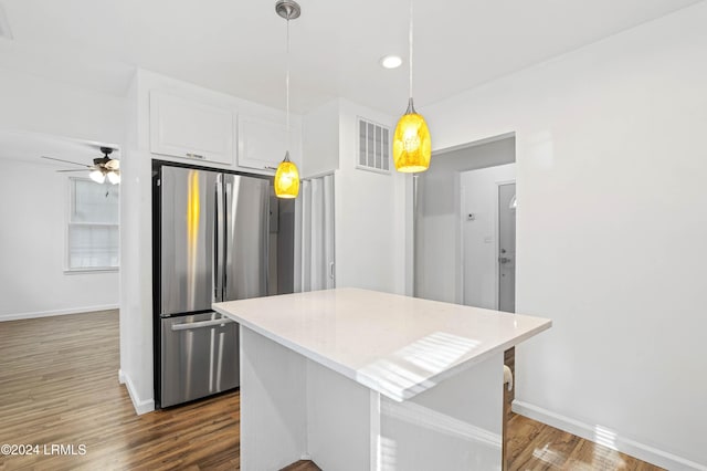 kitchen with stainless steel refrigerator, white cabinetry, hardwood / wood-style floors, a center island, and decorative light fixtures