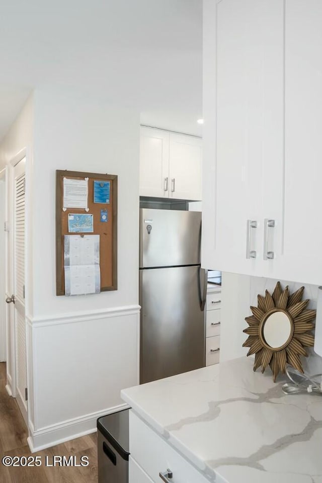 kitchen featuring white cabinetry, freestanding refrigerator, and light stone countertops