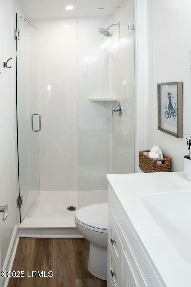 bathroom featuring toilet, vanity, a stall shower, and wood finished floors