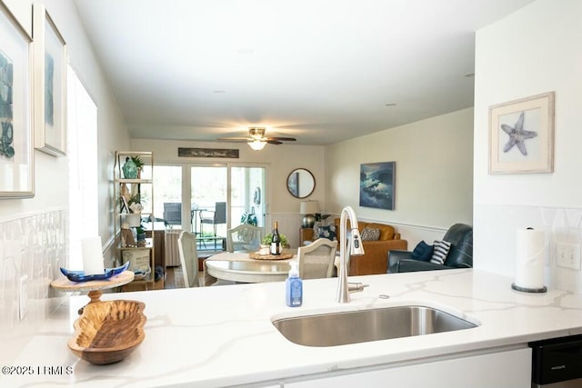 kitchen with light stone counters, open floor plan, a ceiling fan, dishwasher, and a sink