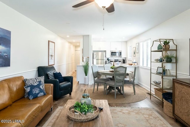 living room featuring light wood-style flooring, ceiling fan, and baseboards