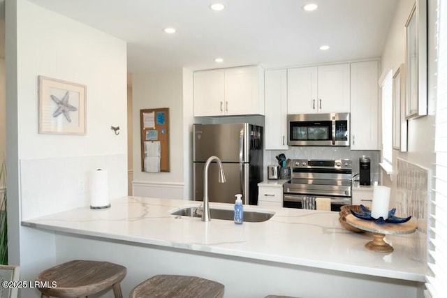 kitchen featuring a sink, a peninsula, white cabinetry, light stone countertops, and stainless steel appliances