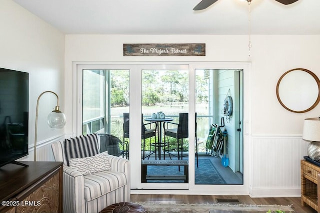 interior space with wood finished floors, a ceiling fan, visible vents, and a wainscoted wall