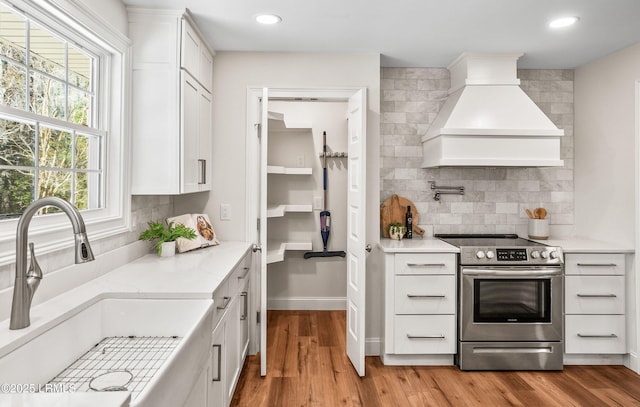 kitchen featuring a sink, custom exhaust hood, stainless steel range with electric stovetop, and white cabinets