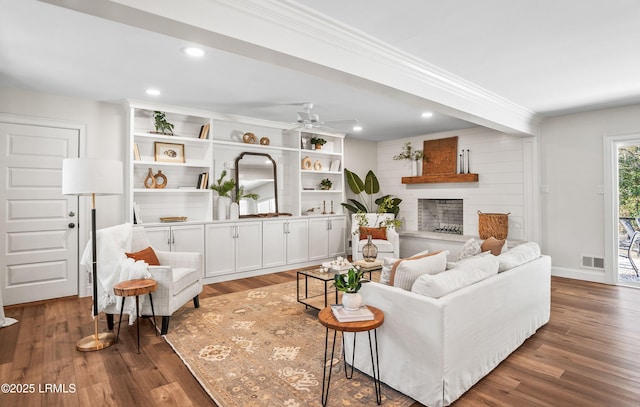 living room featuring a fireplace with raised hearth, dark wood-style flooring, visible vents, and recessed lighting