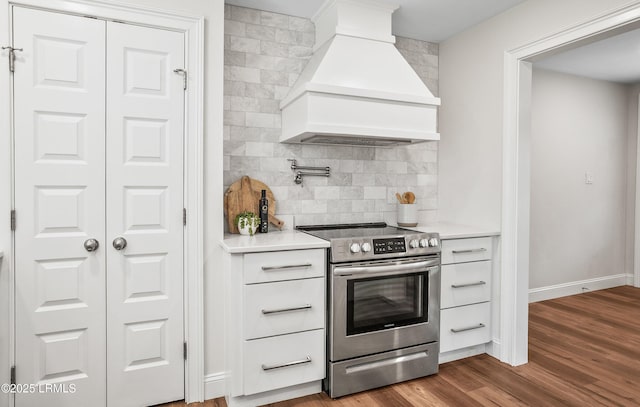 kitchen featuring stainless steel electric stove, light countertops, decorative backsplash, wood finished floors, and premium range hood