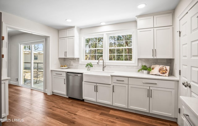 kitchen featuring white cabinets, wood finished floors, light countertops, stainless steel dishwasher, and a sink