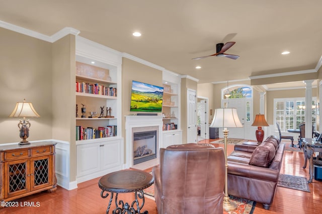 living room with crown molding, built in shelves, light hardwood / wood-style flooring, and decorative columns