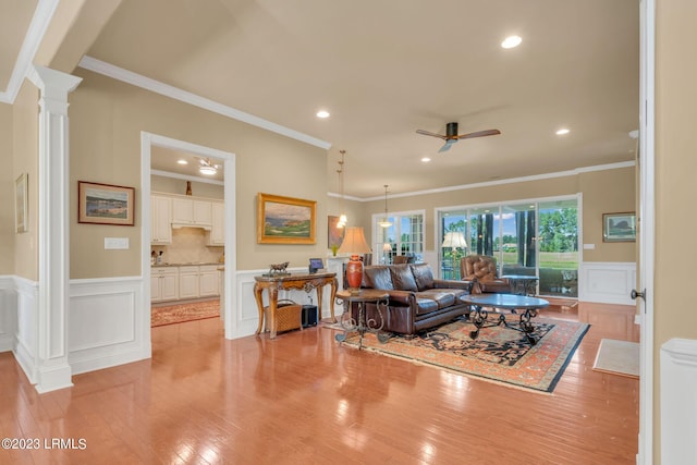 living room featuring decorative columns, crown molding, ceiling fan, and light hardwood / wood-style flooring