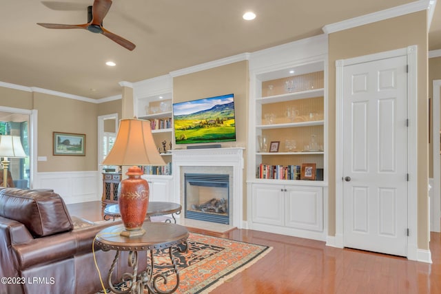 living room featuring hardwood / wood-style floors, crown molding, built in features, and ceiling fan