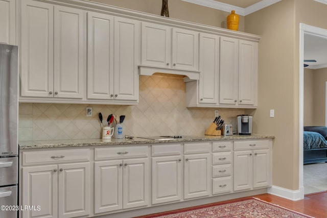 kitchen with tasteful backsplash, white cabinetry, light stone countertops, and stainless steel fridge