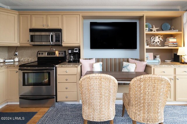 kitchen with appliances with stainless steel finishes, light stone counters, tasteful backsplash, ornamental molding, and light hardwood / wood-style floors