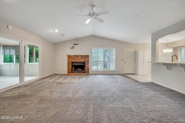 unfurnished living room featuring lofted ceiling, a brick fireplace, ceiling fan with notable chandelier, and light colored carpet