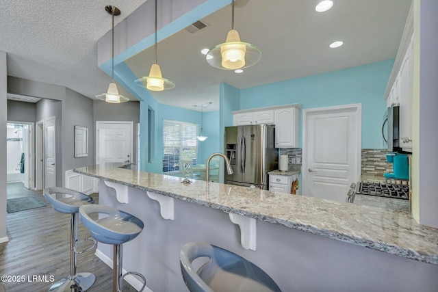 kitchen featuring a peninsula, white cabinets, appliances with stainless steel finishes, a kitchen bar, and pendant lighting