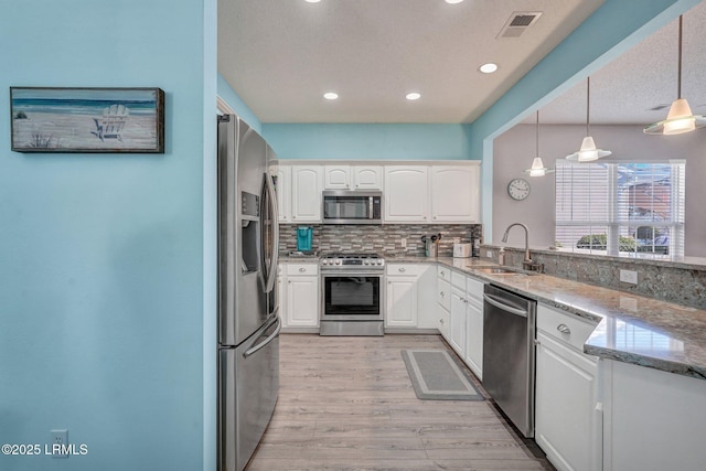 kitchen with stainless steel appliances, white cabinets, a sink, and decorative light fixtures