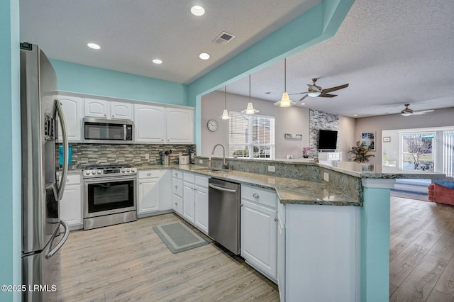 kitchen with a peninsula, white cabinets, open floor plan, appliances with stainless steel finishes, and pendant lighting