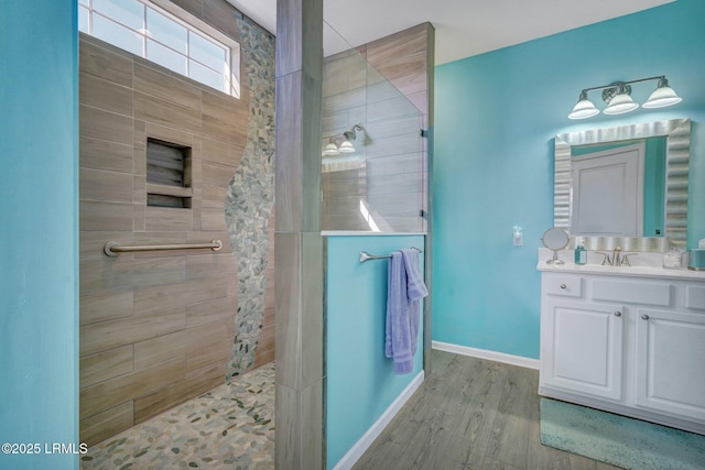 bathroom with wood finished floors, vanity, baseboards, and a walk in shower