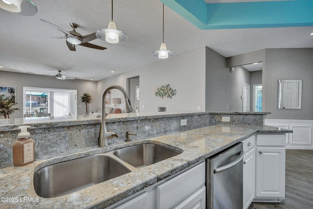 kitchen with decorative light fixtures, stainless steel dishwasher, white cabinets, a sink, and light stone countertops