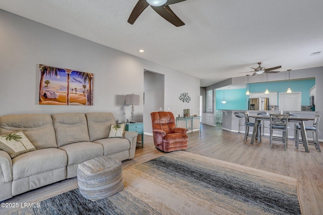 living room featuring a textured ceiling, baseboards, light wood-style flooring, and a ceiling fan