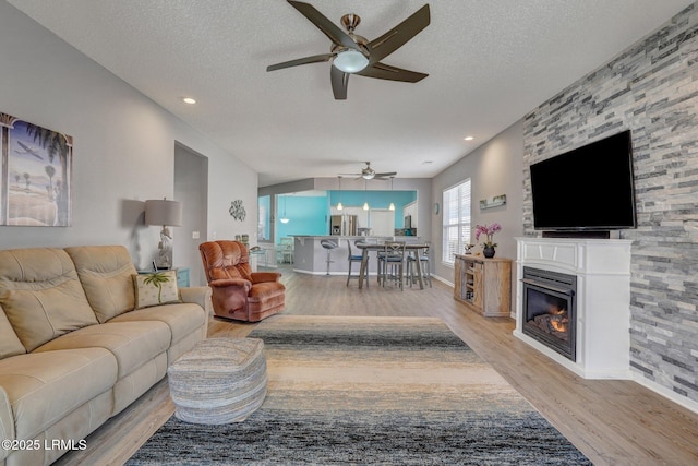 living area featuring recessed lighting, a ceiling fan, a glass covered fireplace, a textured ceiling, and light wood-type flooring