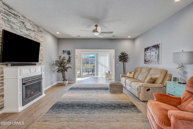 living area with a textured ceiling, ceiling fan, light wood-type flooring, and a glass covered fireplace