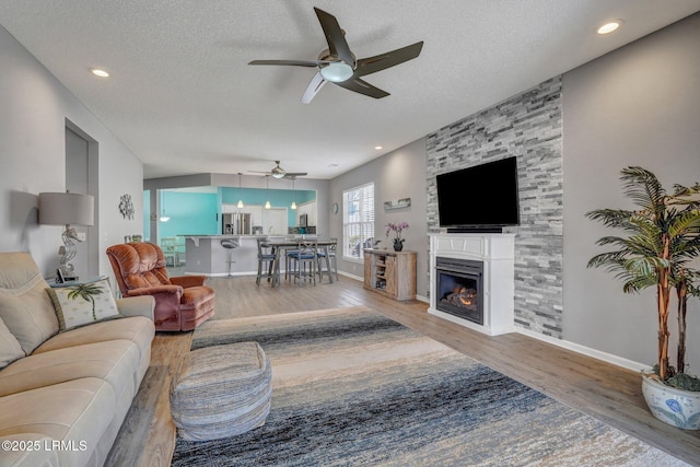 living area featuring a textured ceiling, baseboards, wood finished floors, and a glass covered fireplace