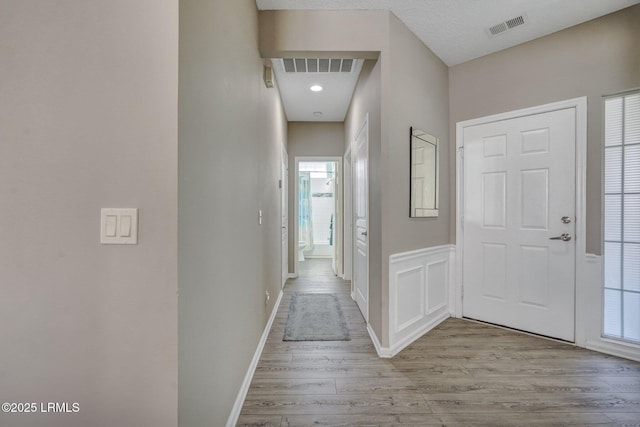 hallway with light wood-style floors, visible vents, a decorative wall, and a wainscoted wall