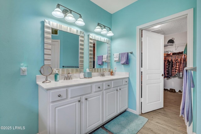 full bath featuring wood finished floors, a spacious closet, double vanity, and a sink