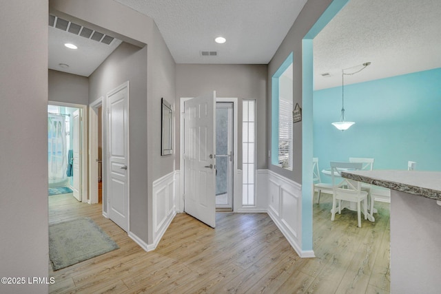 hall with light wood-style floors, a textured ceiling, and wainscoting