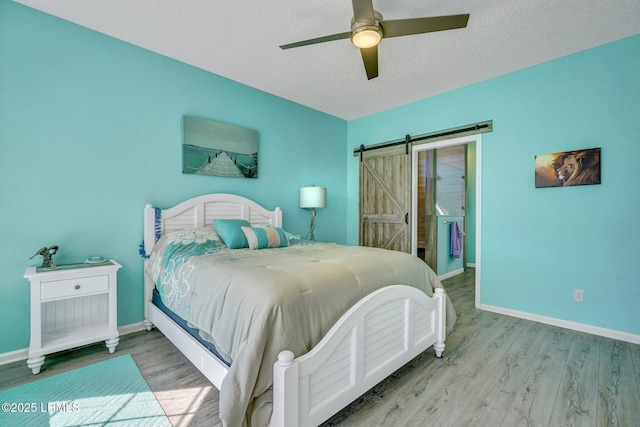 bedroom with a barn door, baseboards, a ceiling fan, light wood-style flooring, and a textured ceiling