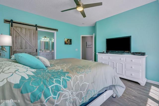 bedroom with a barn door, ensuite bathroom, ceiling fan, a textured ceiling, and wood finished floors