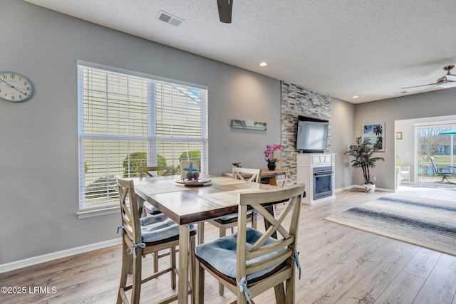 dining space with a large fireplace, visible vents, ceiling fan, a textured ceiling, and light wood-style floors