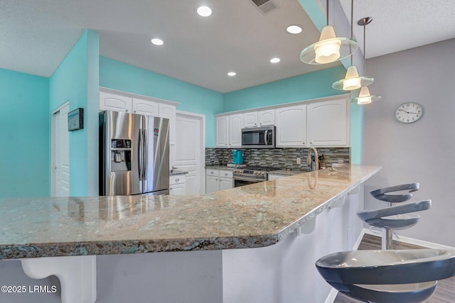 kitchen featuring decorative light fixtures, a breakfast bar area, appliances with stainless steel finishes, white cabinetry, and a peninsula