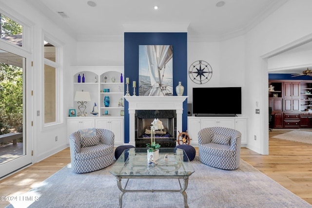 living room featuring ceiling fan, a high end fireplace, built in features, and light wood-type flooring