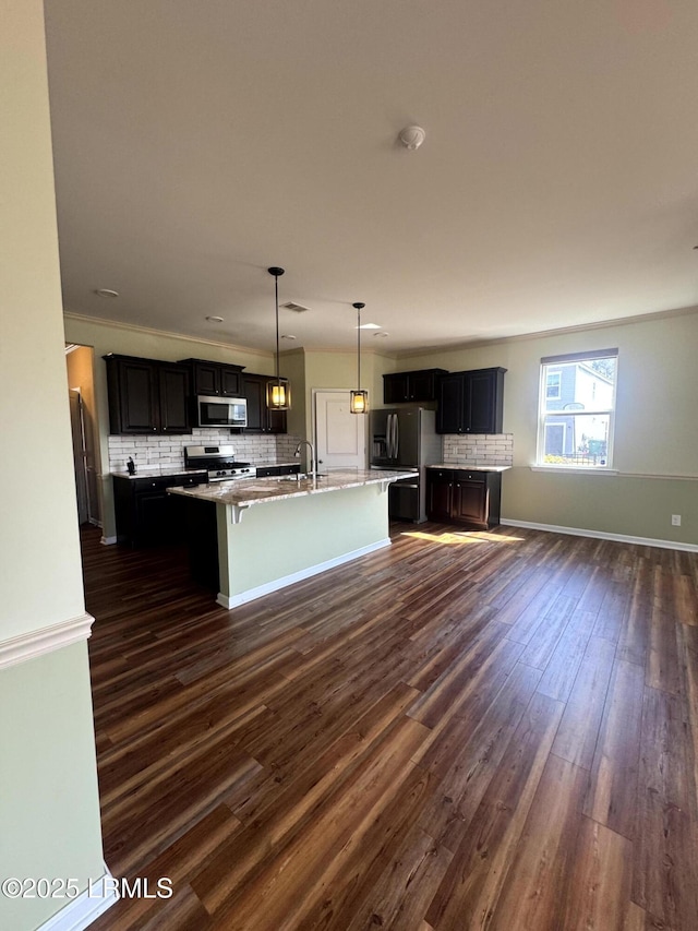 kitchen featuring dark wood-style flooring, backsplash, stainless steel appliances, and a kitchen island with sink