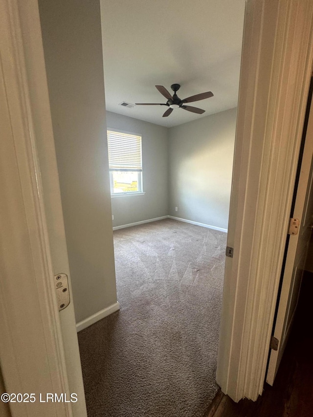 carpeted spare room with visible vents, baseboards, and a ceiling fan