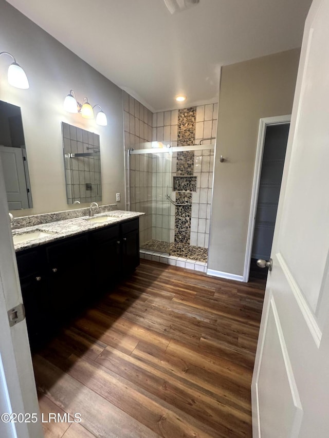 bathroom featuring double vanity, wood finished floors, a stall shower, and a sink