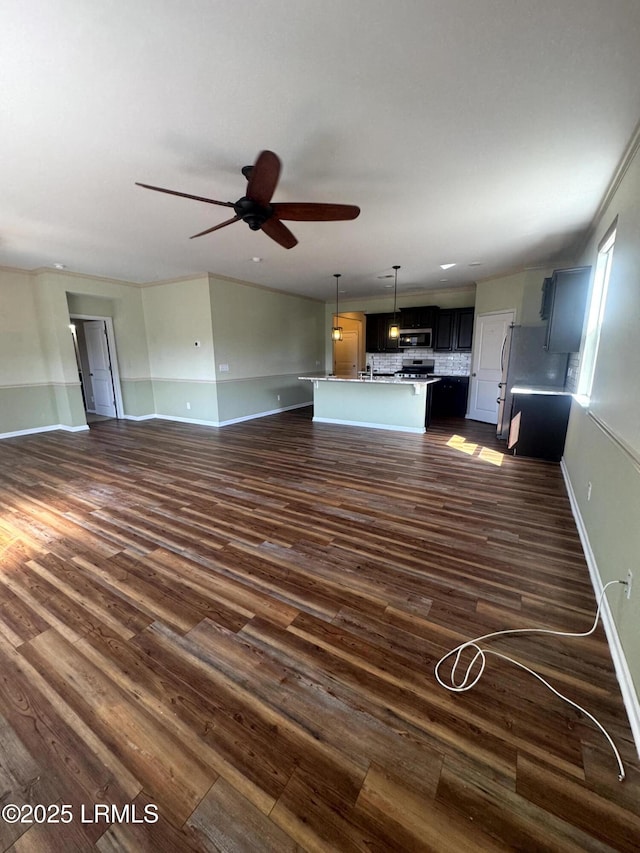 unfurnished living room with dark wood-type flooring, a ceiling fan, and baseboards